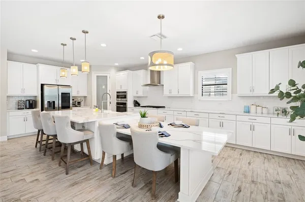 a large kitchen with kitchen island a stove a sink a refrigerator and white cabinets with wooden floor