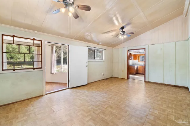 an empty room with chandelier fan and windows