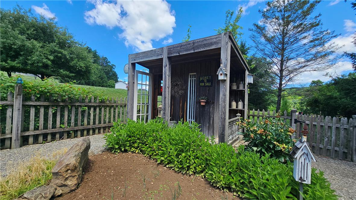 585 Buttermilk Road Hellertown, PA 18055 - Photo 53 of 82 A charming rustic shed with a picket fence, set against a backdrop of rolling hills and blue skies.