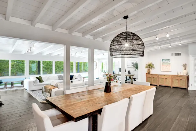 a dining room with wooden floor windows and kitchen view