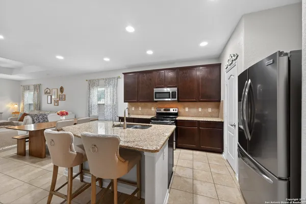 a kitchen with stainless steel appliances granite countertop a refrigerator a sink a stove a dining table and chairs