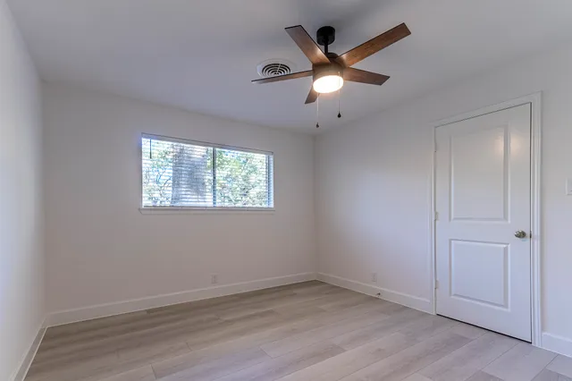 an empty room with wooden floor ceiling fan and windows