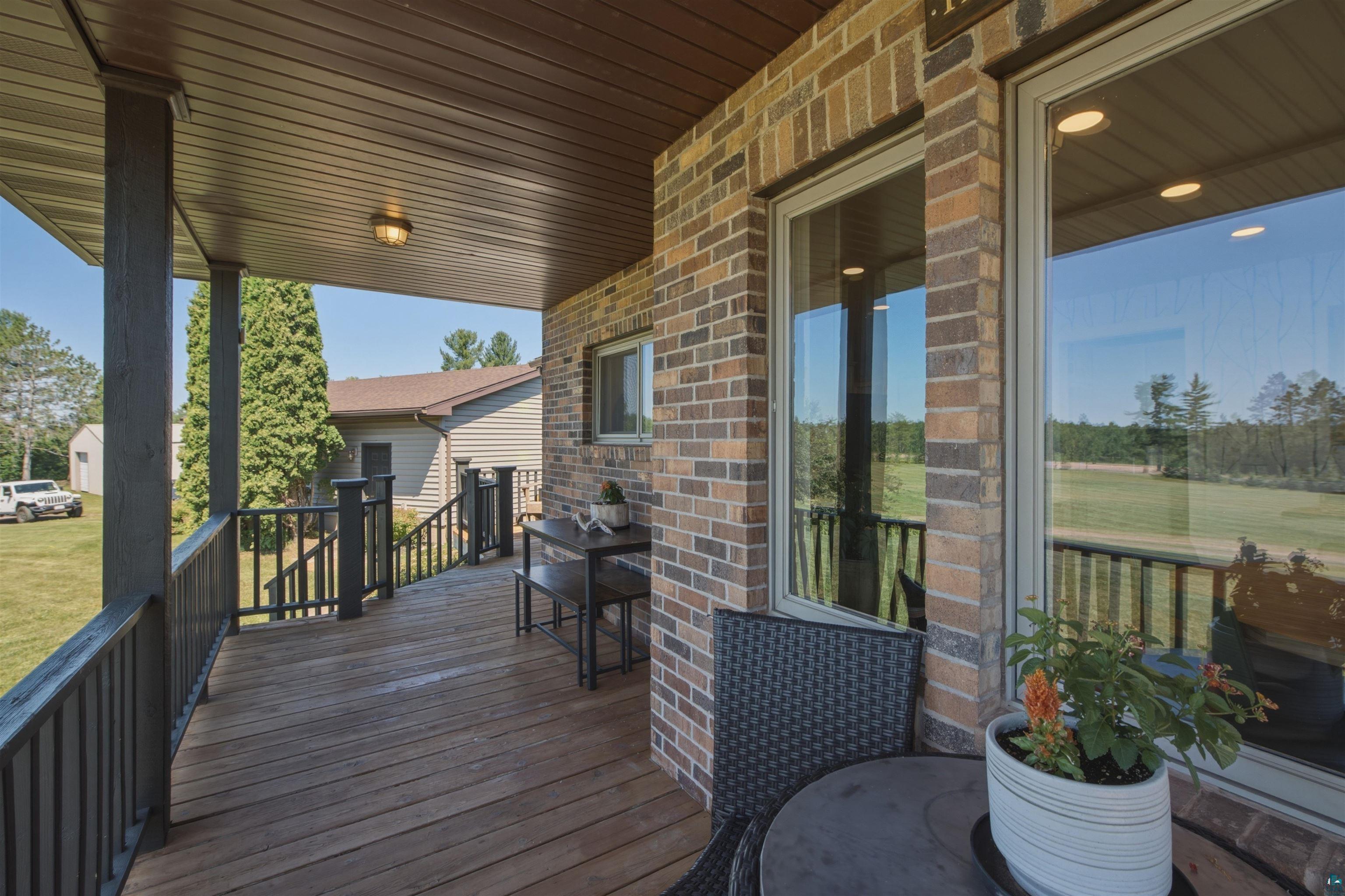 64260 Jolma Road Ashland, WI 54806 - Photo 26 of 35 Covered wood-finish porch featuring brick wall accents, dark wood-finish columns, dark railings, and exterior lighting
