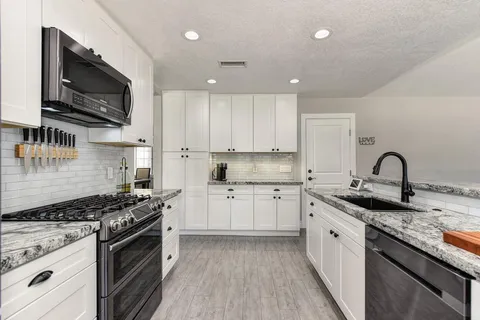 a kitchen with granite countertop a sink a stove top oven and wooden floor