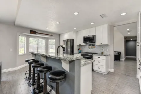 a kitchen with stainless steel appliances kitchen island granite countertop a stove top oven a sink a dining table and chairs with wooden floor
