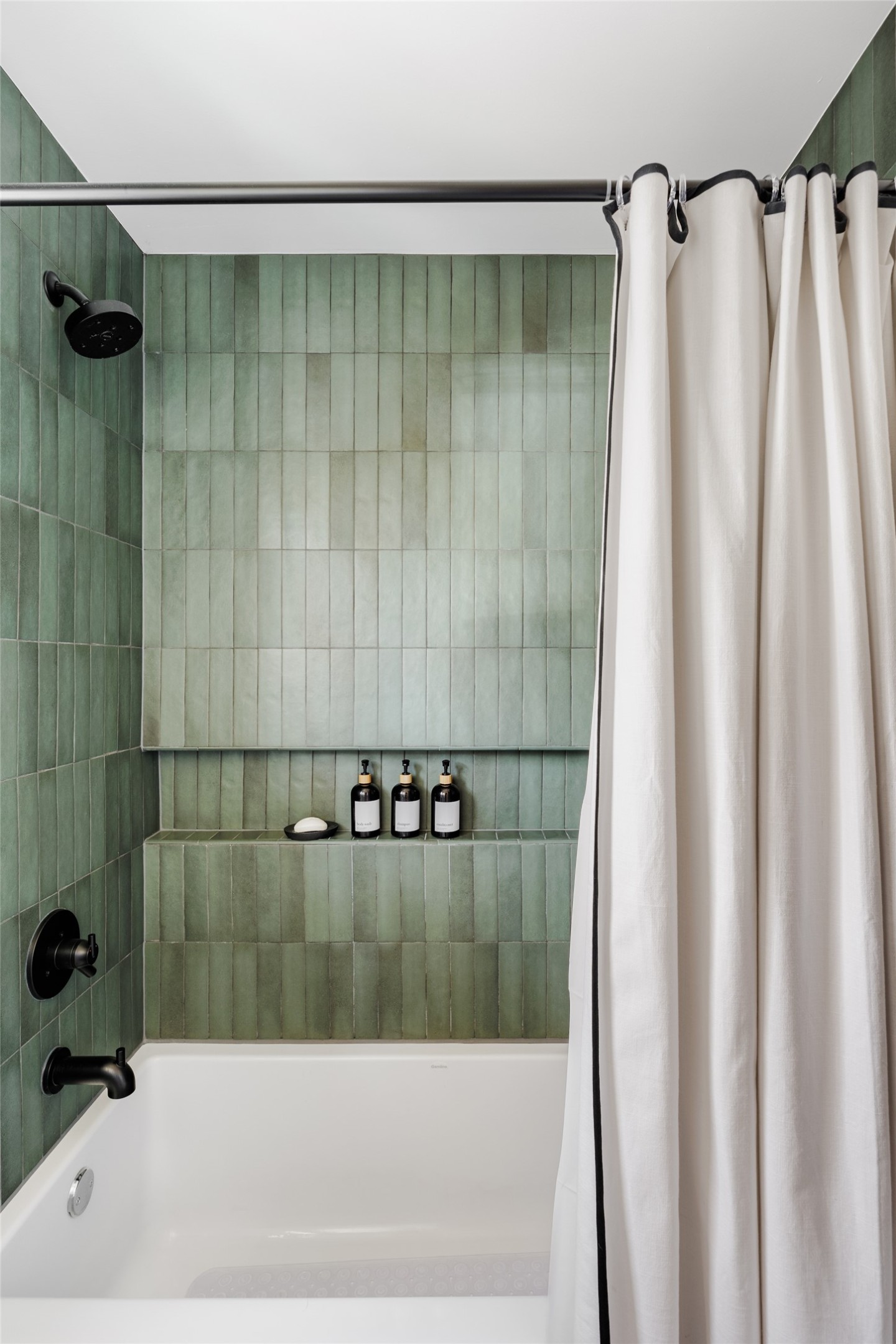 106 Comal Street Austin, TX 78702 - Photo 28 of 40 A deep soaking tub with sleek black fixtures and rich green tiled walls offers a tranquil bathing experience.
