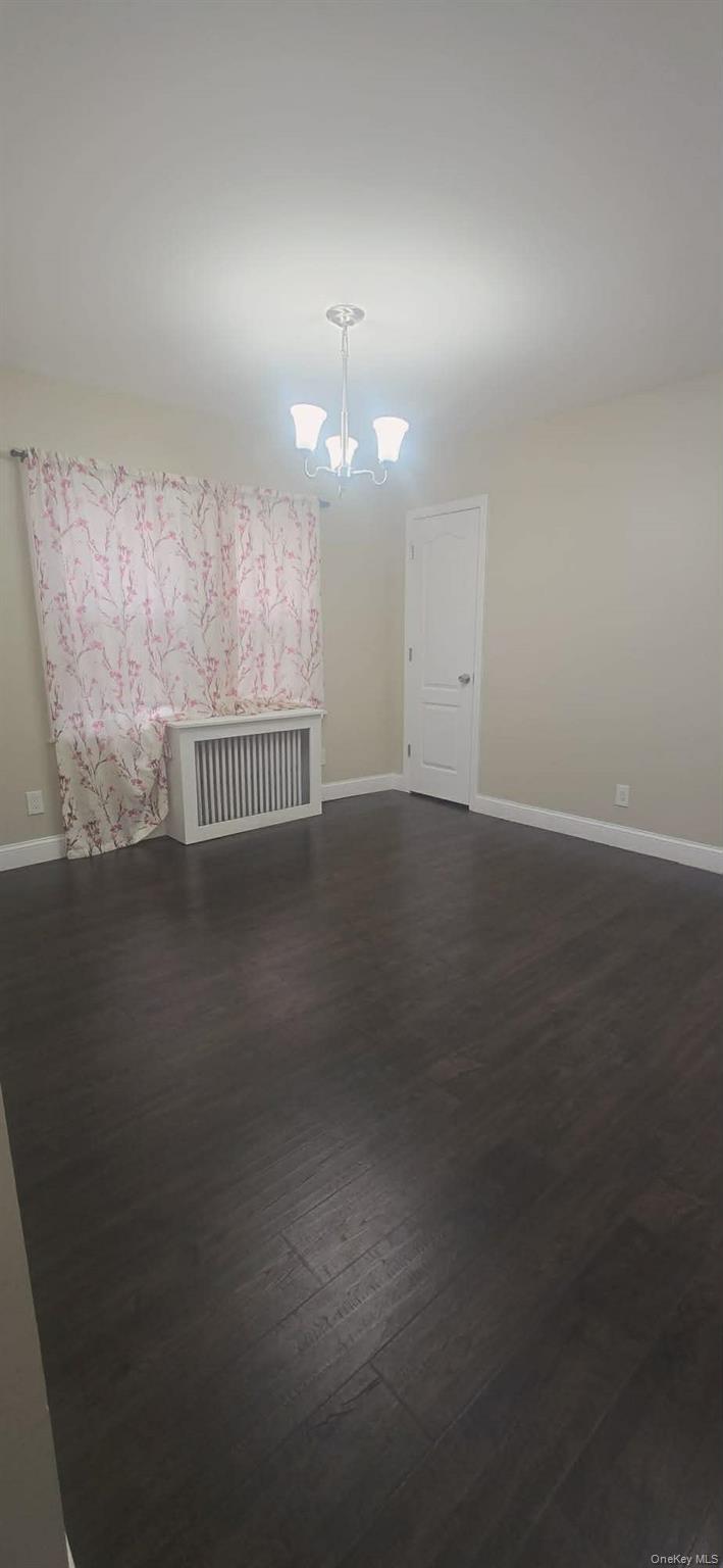 Unfurnished room with dark wood finished floors and a chandelier