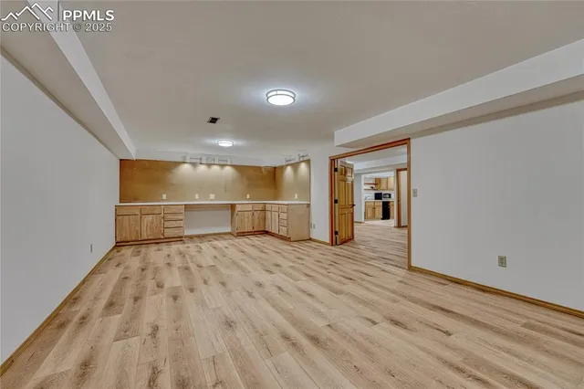 a view of an empty room with wooden floor and kitchen