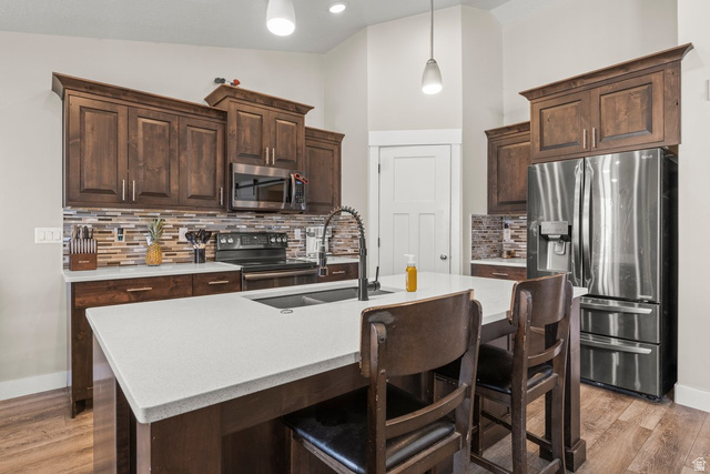 463 South Trejo Ridge Road Grantsville, UT 84029 - Photo 5 of 22 Modern kitchen featuring a white quartz-finish island with integrated sink, dark wood-finish cabinetry, stainless steel appliances, and a mosaic tile backsplash