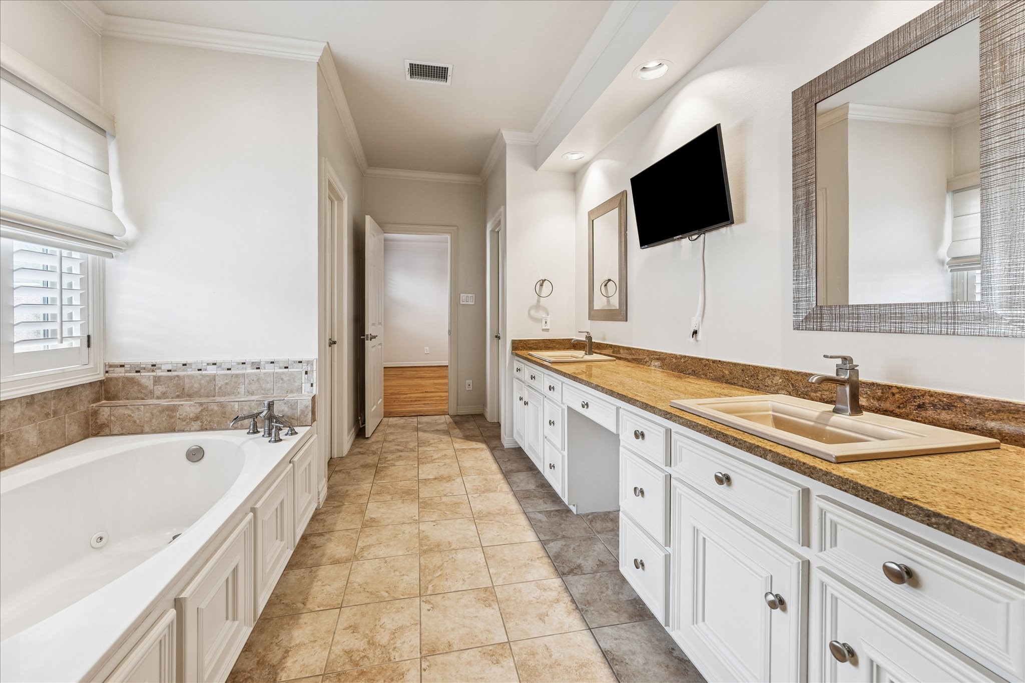 5823 Augusta Court Houston, TX 77057 - Photo 24 of 44 The primary bathroom features a large soaking tub and dual sinks with granite countertops. It has ample storage with white cabinetry, a wall-mounted TV, and a neutral tile floor, offering a bright and elegant space.