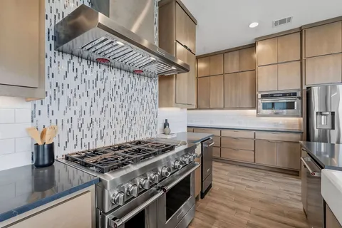 a kitchen with stainless steel appliances granite countertop a stove a sink dishwasher and refrigerator with wooden floor