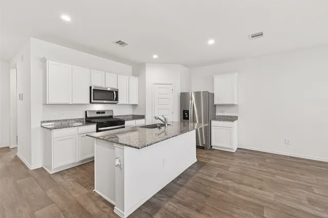 a kitchen with stainless steel appliances a sink stove refrigerator and white cabinets with wooden floor