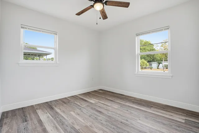 an empty room with wooden floor chandelier fan and windows