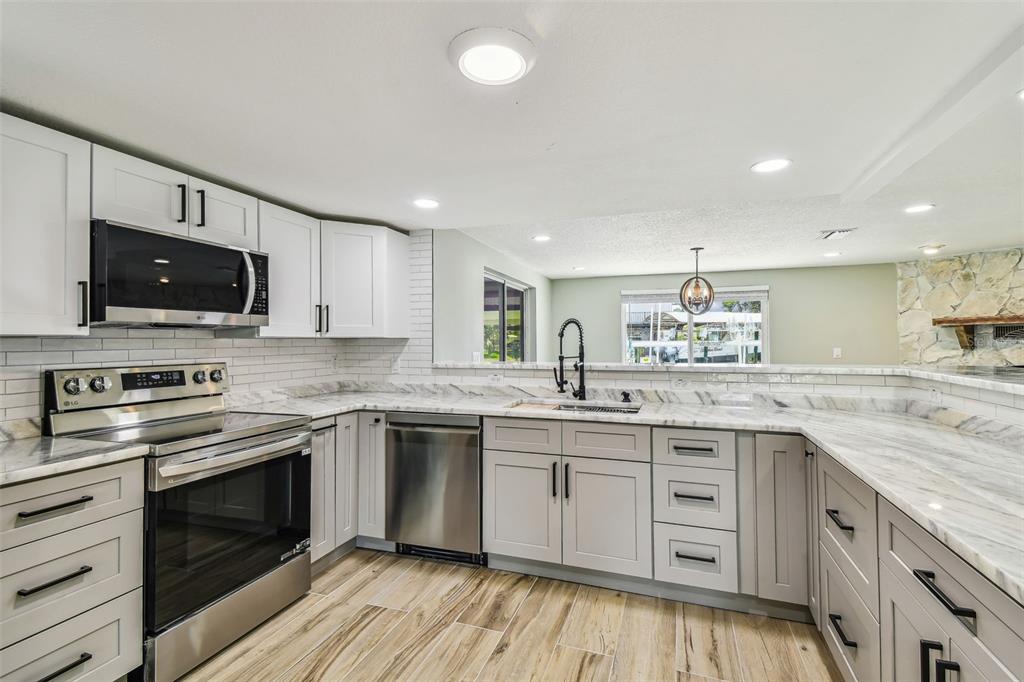 13909 Berkowitz Avenue Hudson, FL 34667 - Photo 12 of 91 a kitchen with stainless steel appliances granite countertop a stove top oven a sink dishwasher a dining table and chairs with wooden floor