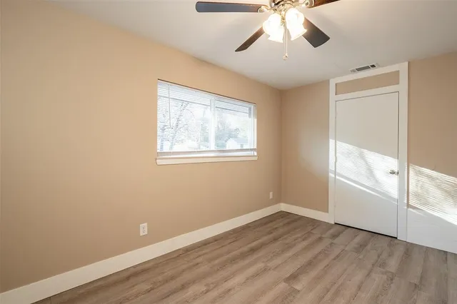 an empty room with wooden floor chandelier fan and windows