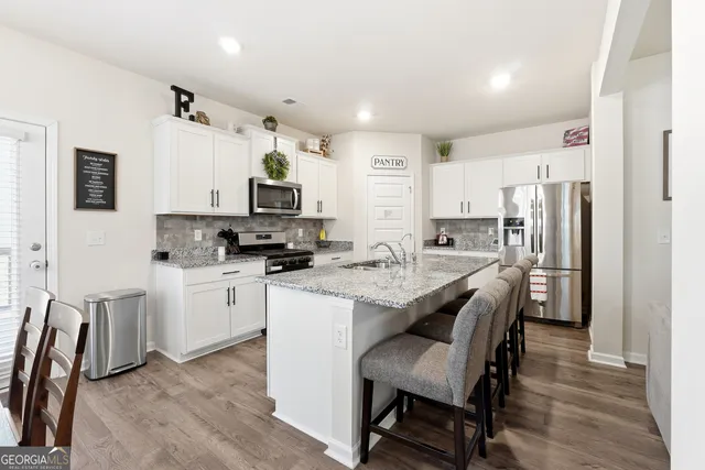 a kitchen with stainless steel appliances a stove a sink dishwasher a refrigerator a stove a dining table and chairs with wooden floor