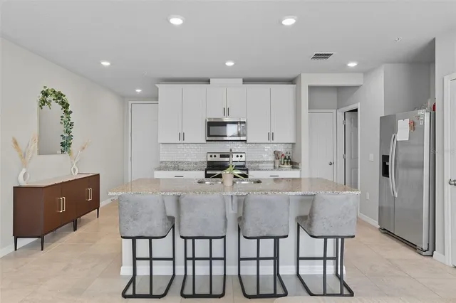 a kitchen with stainless steel appliances granite countertop a stove a refrigerator and a dining table with white cabinets