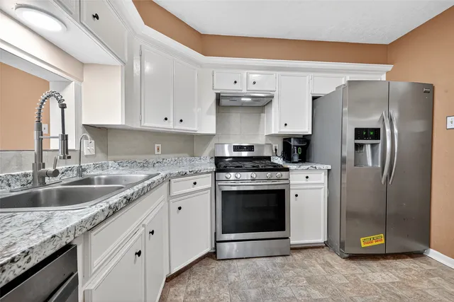 a kitchen with granite countertop a sink stainless steel appliances and white cabinets