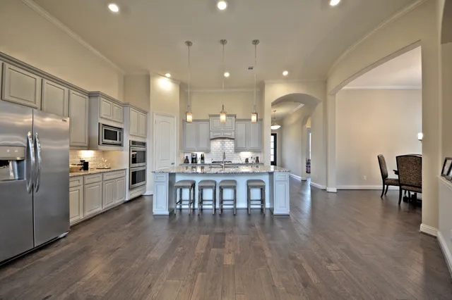 a kitchen with stainless steel appliances a refrigerator a stove top oven a sink dishwasher a dining table and chairs with wooden floor