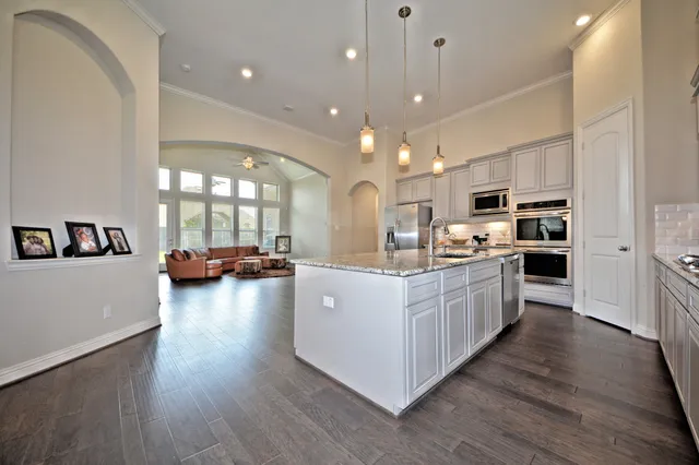 a large white kitchen with kitchen island a large counter top and stainless steel appliances
