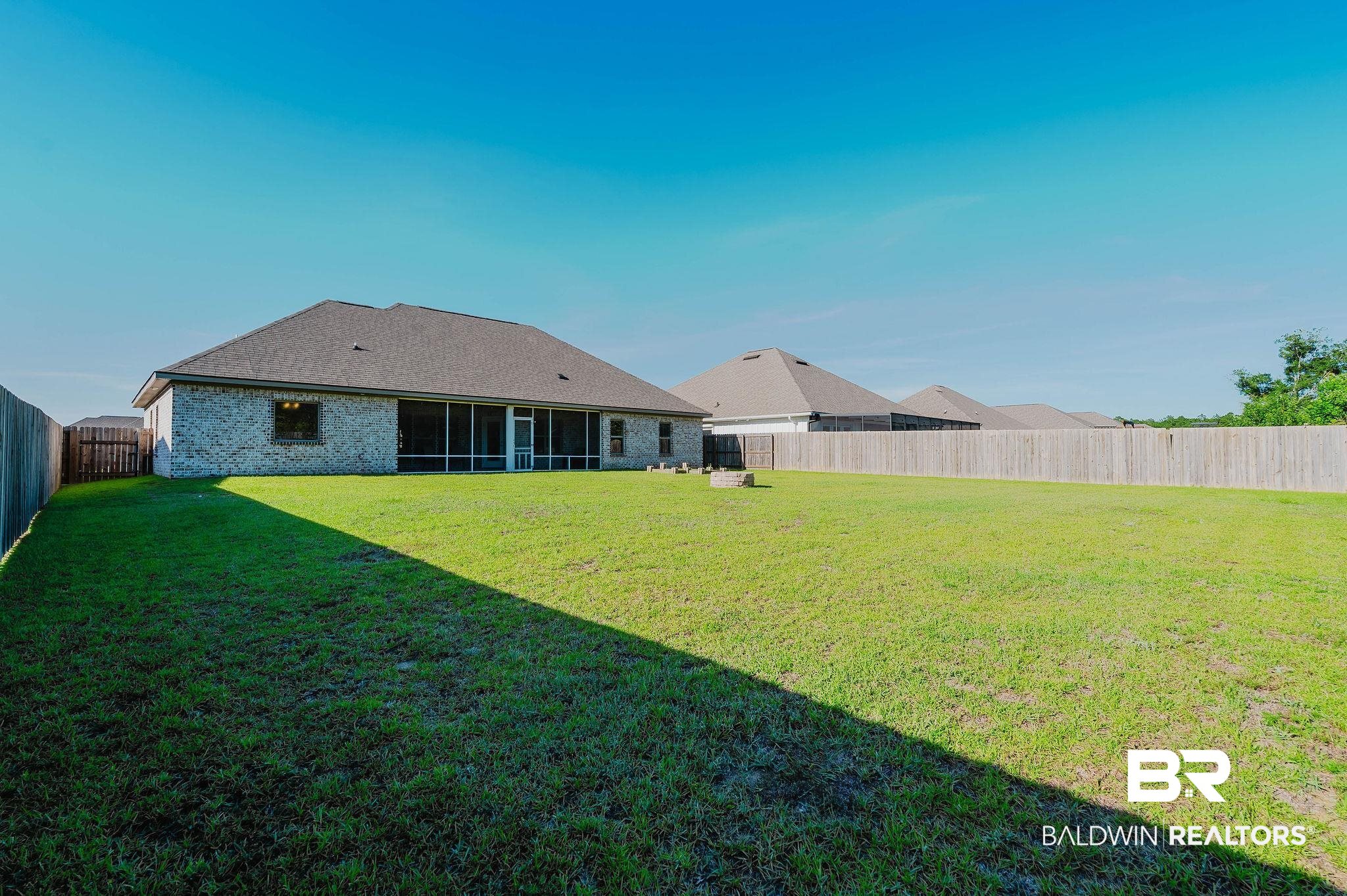 7872 Calverton Street Foley, AL 36535 - Photo 60 of 76 Spacious backyard featuring a full privacy fence, expansive green lawn, and a light brick exterior home with a screened-in patio