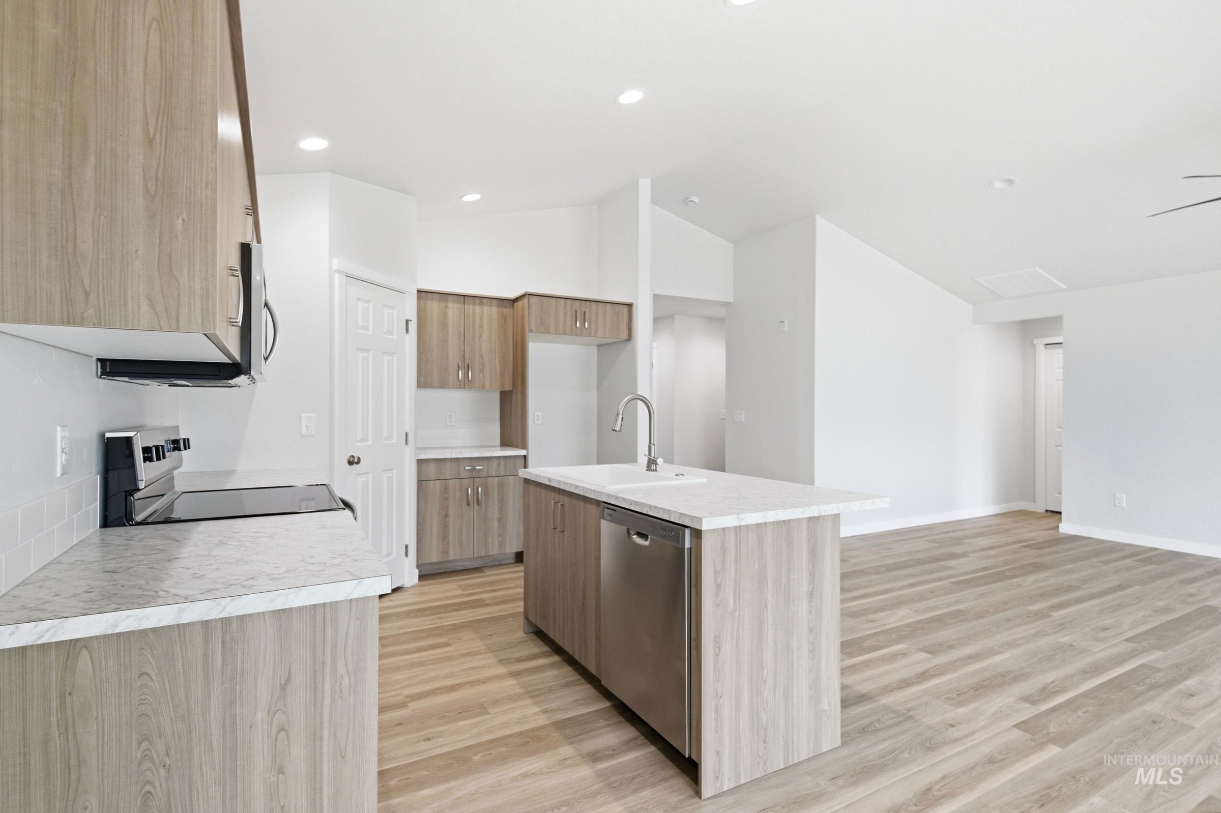 13735 Inman Court Caldwell, ID 83607 - Photo 7 of 20 Kitchen with light countertops, a kitchen island with sink, light wood-style floors, stainless steel appliances, and vaulted ceiling