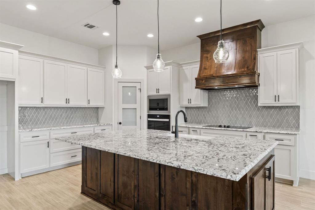 8017 Rnch Vw Place Springtown, TX 76082 - Photo 7 of 18 Chef's kitchen featuring white cabinetry, quartz countertops, stainless steel double wall ovens, a dark wood island with stone countertop surface, pendant lighting, geometric tile backsplash, and wood-finish flooring throughout