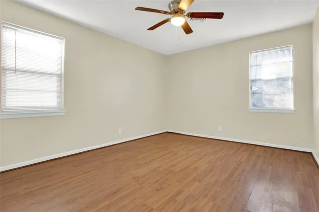 an empty room with wooden floor fan and windows