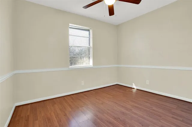 an empty room with wooden floor chandelier fan and windows
