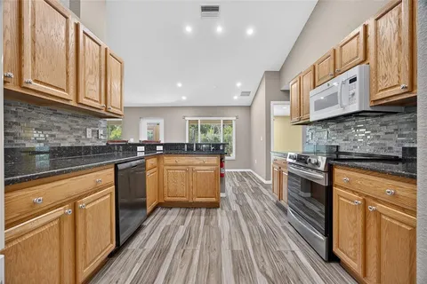 a kitchen with stainless steel appliances granite countertop wooden cabinets a stove top oven a sink and dishwasher with wooden floor