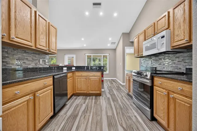 a kitchen with stainless steel appliances granite countertop wooden cabinets a stove top oven a sink and dishwasher with wooden floor