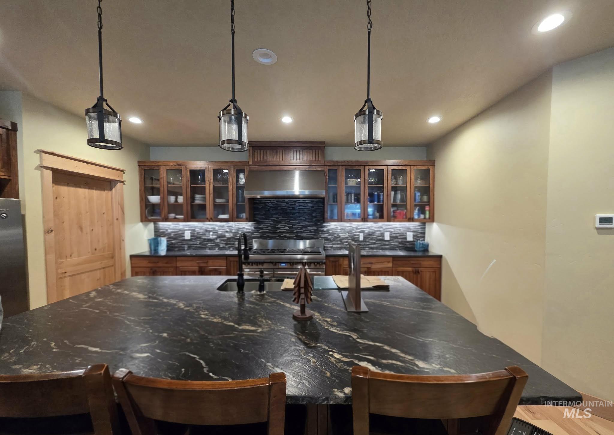 36 Kevins Way Garden Valley, ID 83622 - Photo 13 of 50 Bar area featuring glass insert cabinets, hanging light fixtures, recessed lighting, dark stone countertops, and wall chimney exhaust hood