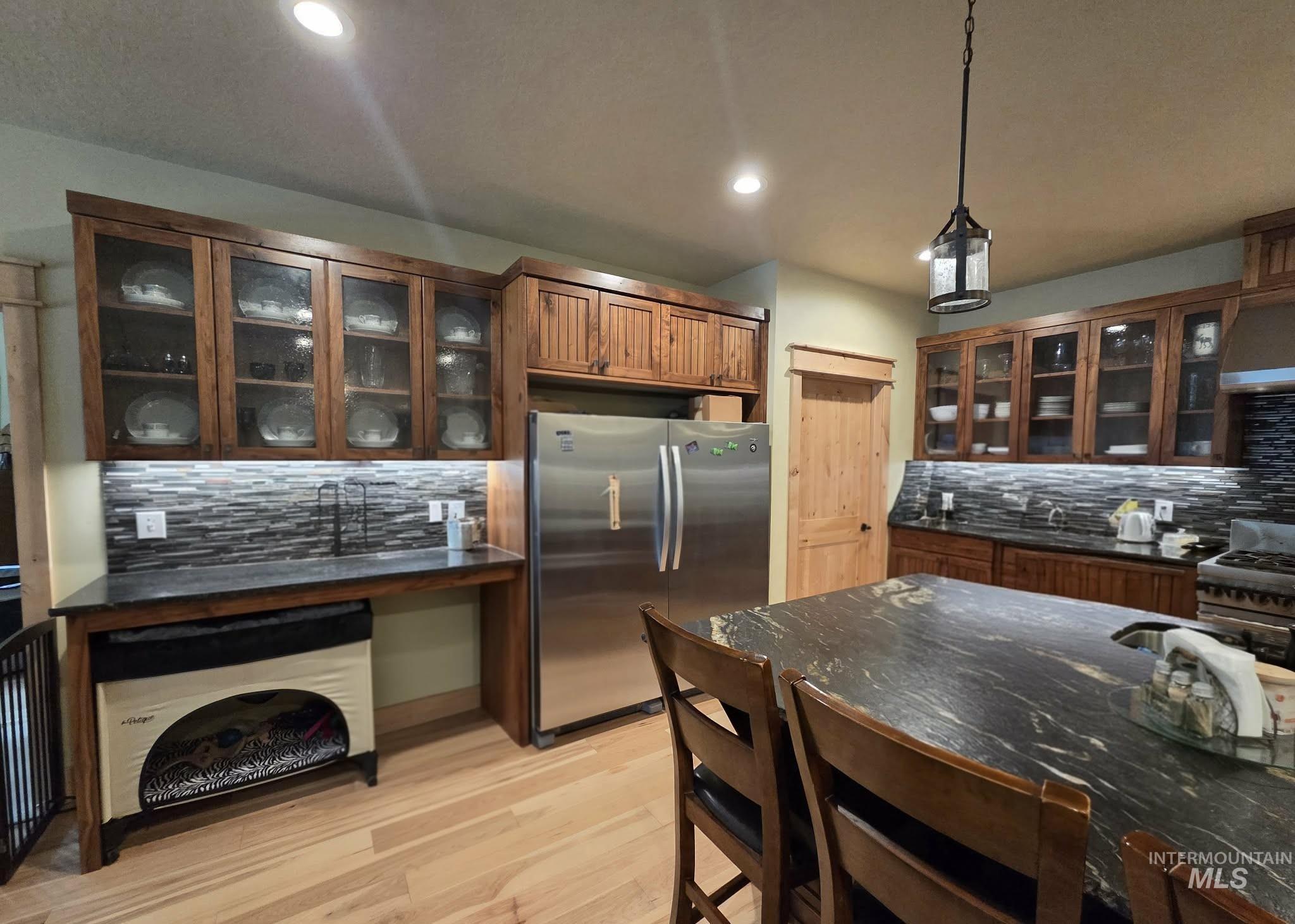 36 Kevins Way Garden Valley, ID 83622 - Photo 14 of 50 Kitchen featuring glass insert cabinets, decorative backsplash, appliances with stainless steel finishes, hanging light fixtures, and light wood-style floors