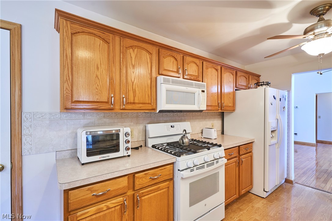 1963 Haines Road Madison, OH 44057 - Photo 16 of 34 Kitchen featuring wood cabinetry, light-toned countertops, tile backsplash, and a ceiling fan with integrated lighting