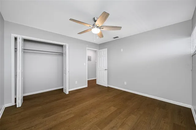 a view of an empty room with wooden floor and a ceiling fan