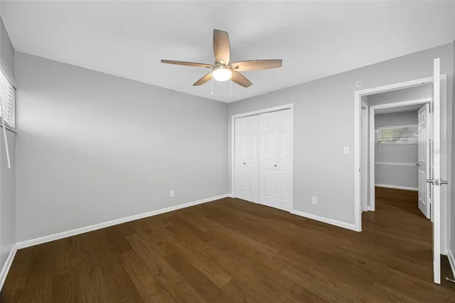 an empty room with wooden floor ceiling fan and a window