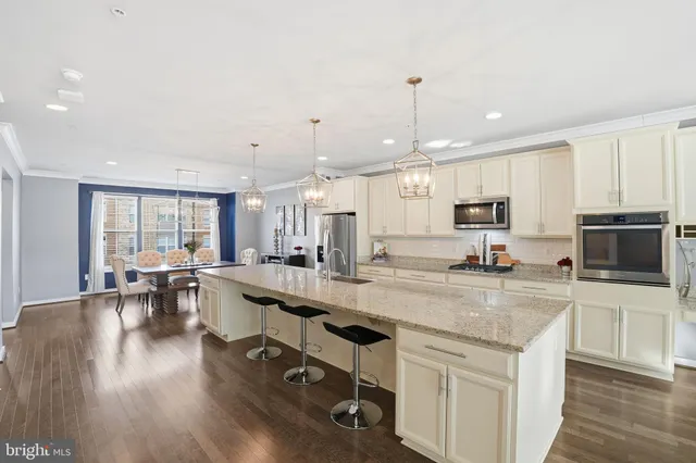 a kitchen with stainless steel appliances granite countertop a stove top oven a sink a dining table and chairs with wooden floor