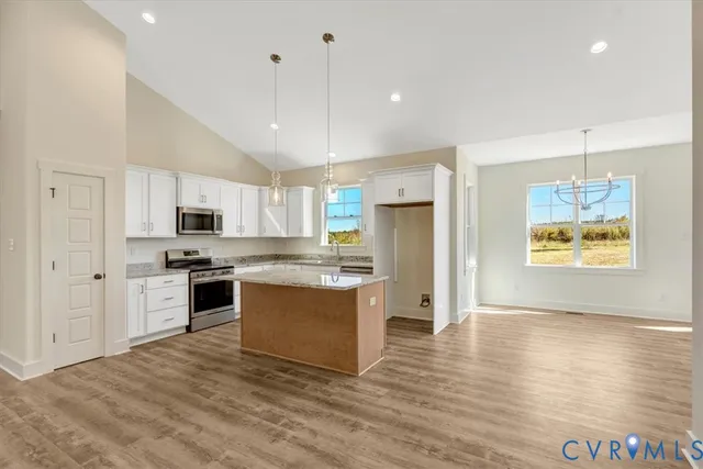 a large kitchen with stainless steel appliances granite countertop a stove a sink a refrigerator and white cabinets with wooden floor