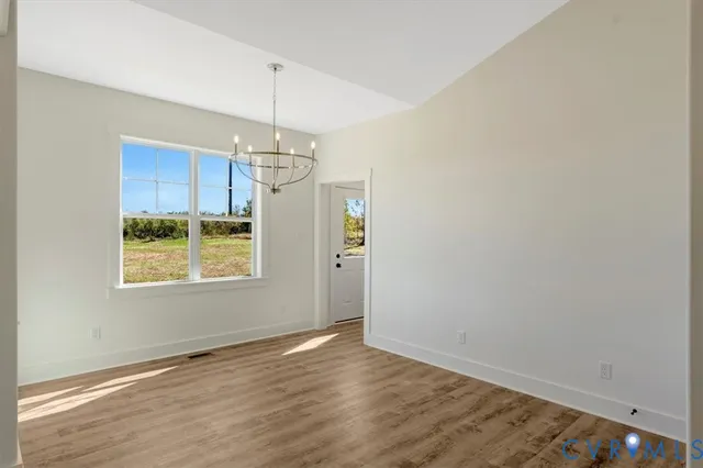 an empty room with wooden floor chandelier and windows