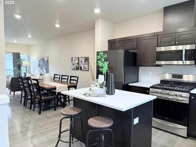 a open kitchen with stainless steel appliances kitchen island granite countertop a stove a refrigerator a white table and chairs