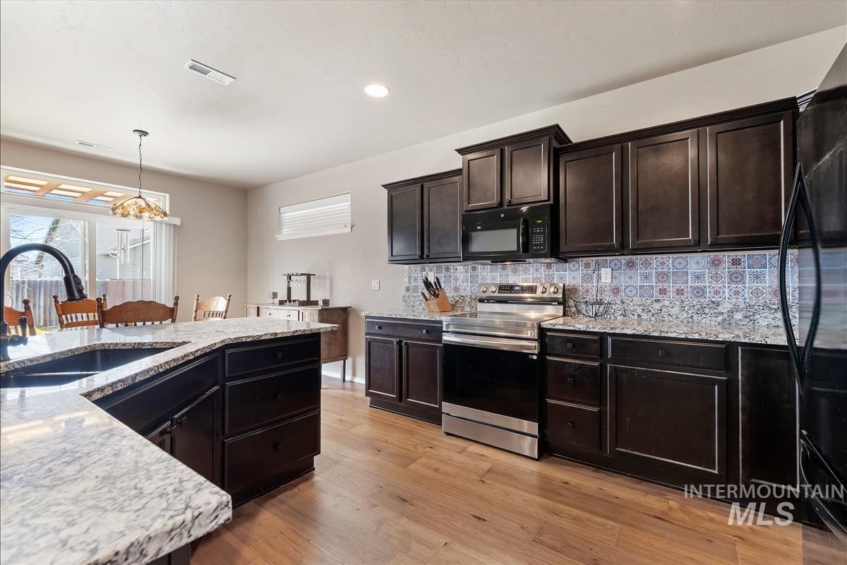 6308 South Kelso Way Boise, ID 83709 - Photo 12 of 35 Kitchen with black appliances, hanging light fixtures, light stone countertops, light wood finished floors, and tasteful backsplash
