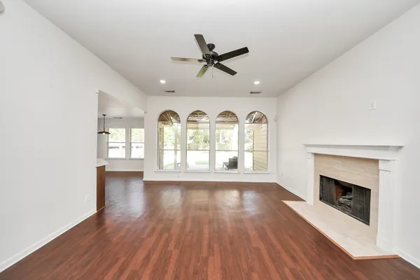 an empty room with wooden floor a fireplace a ceiling fan and windows