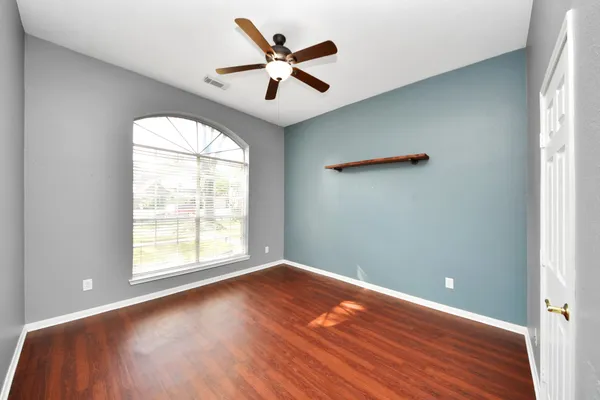 an empty room with wooden floor fan and windows