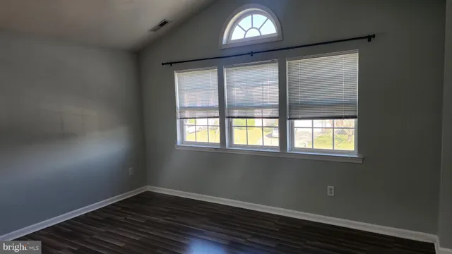 an empty room with wooden floor fan and windows