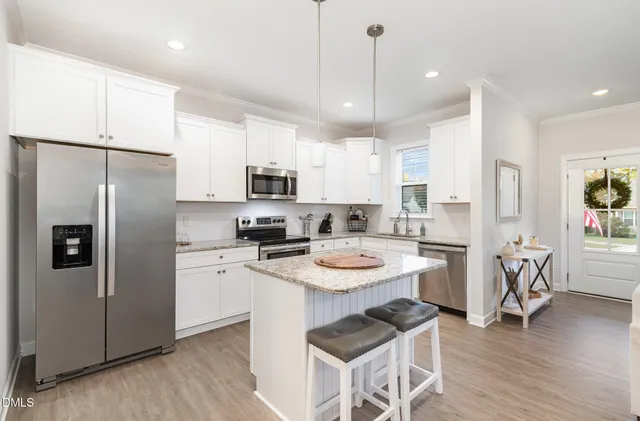 a kitchen with stainless steel appliances kitchen island a refrigerator a stove a sink a dining table and chairs with wooden floor