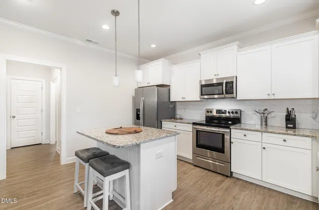 a kitchen with granite countertop a sink stove a refrigerator and white cabinets with wooden floor