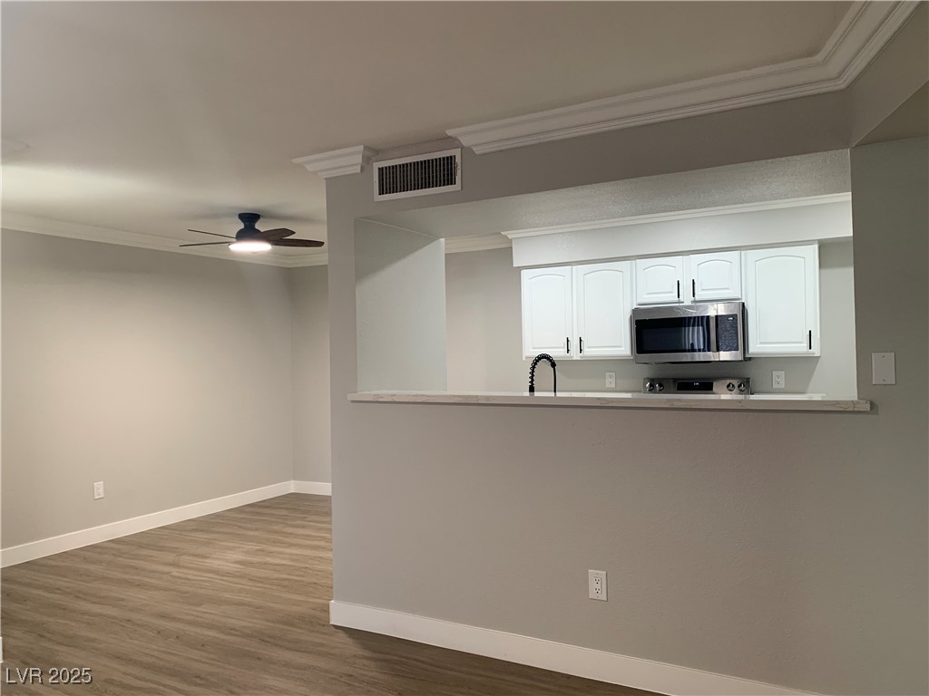8101 West Flamingo Road, Unit 1102 Las Vegas, NV 89147 - Photo 20 of 54 Kitchen featuring stainless steel microwave, ornamental molding, white cabinetry, wood finished floors, and a ceiling fan