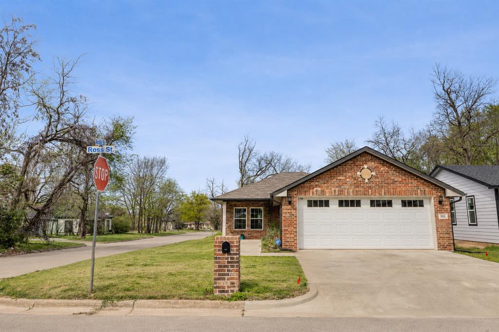 101 Ross Street Sulphur Springs, TX 75482 - Photo 2 of 30 Brick facade home featuring a gable roof, an attached two-car garage with transom windows, a concrete driveway, and a manicured front lawn