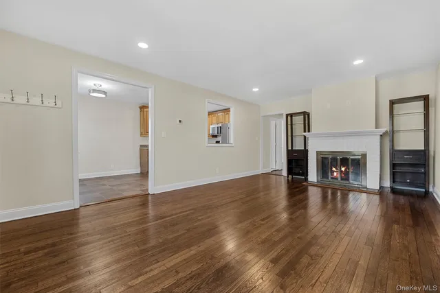 a view of an empty room with wooden floor fireplace and a window