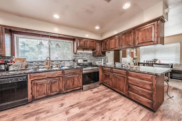 a kitchen with stainless steel appliances granite countertop wooden cabinets a sink a stove a refrigerator and island with wooden floors